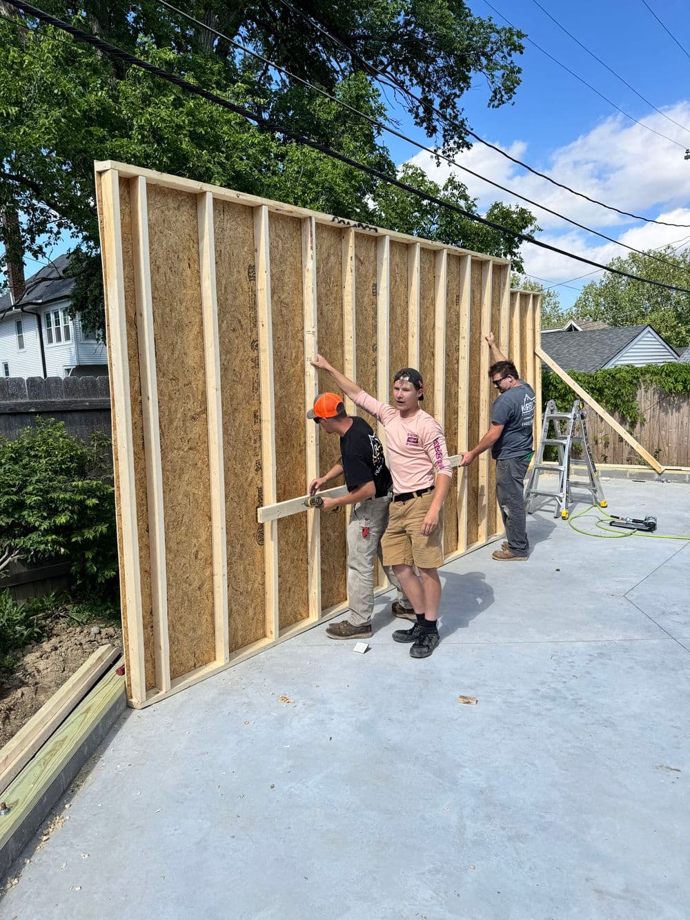 Three construction workers raising a wooden wall frame on a home construction site.