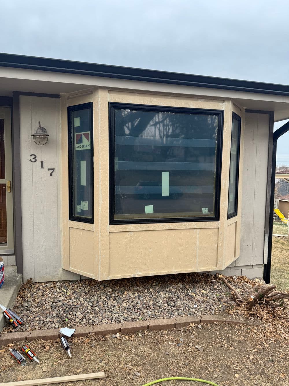 Newly installed bay window on a home exterior with beige siding and stone landscaping.