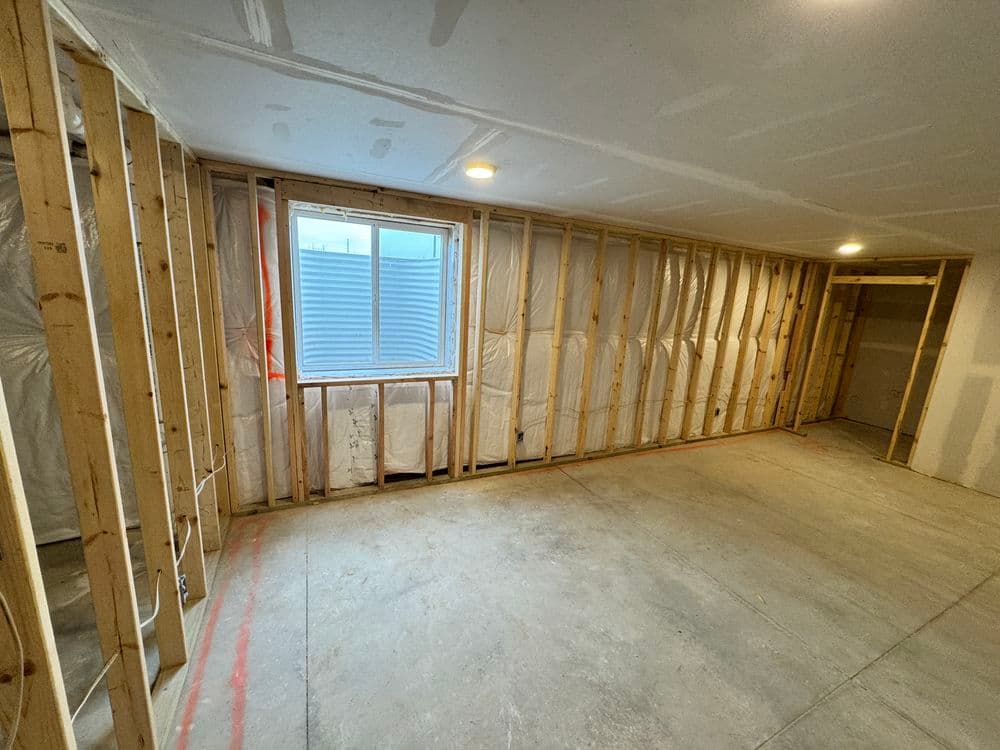Interior of a partially finished basement with exposed framing, drywall, and a window.