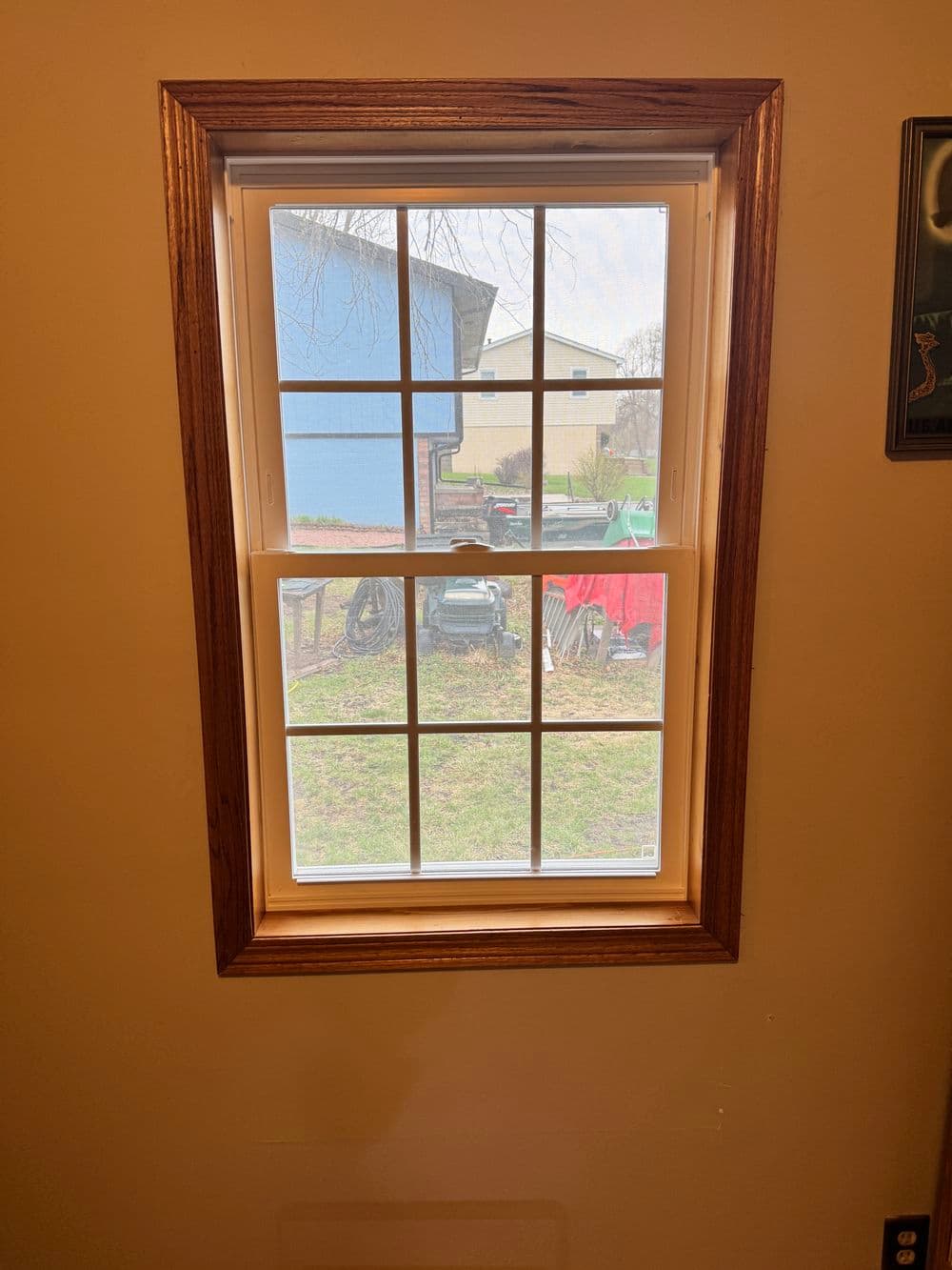 Window with wooden frame, showing outdoor view of blue building and green yard.