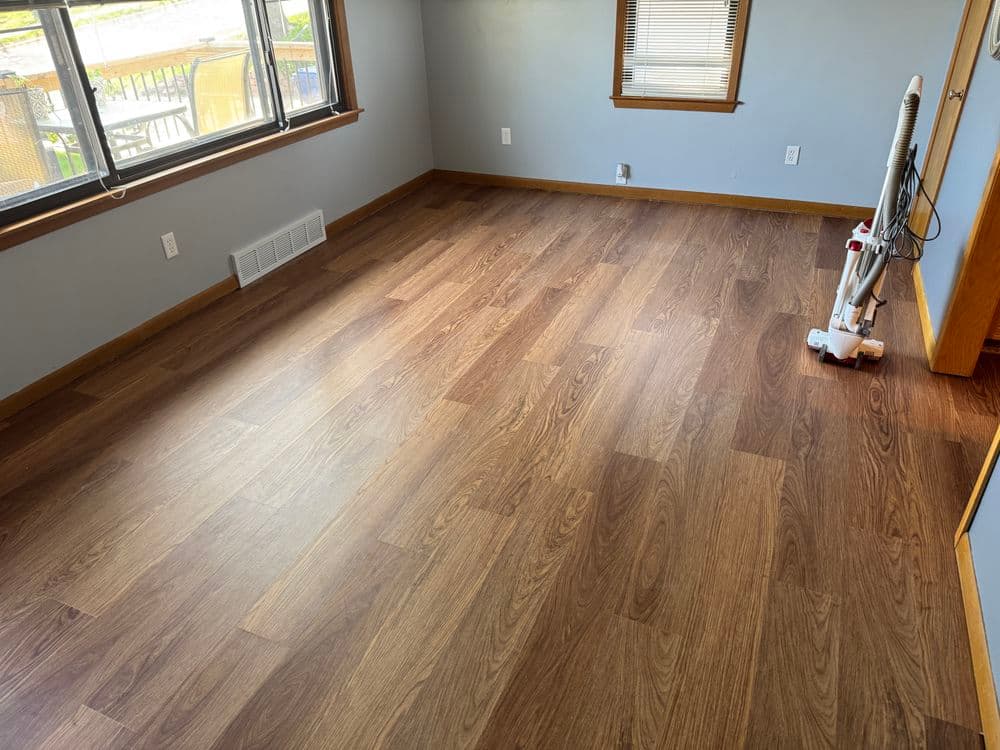 Empty room with new wood laminate flooring and large windows for natural light.