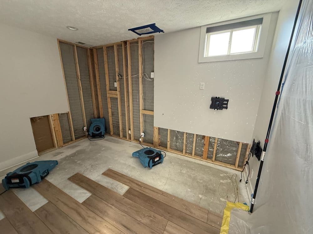 Water-damaged room undergoing renovation with drying equipment and exposed walls.
