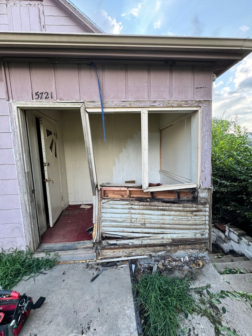 Damaged entrance of a house with peeling paint and exposed wood, showcasing neglect and decay.