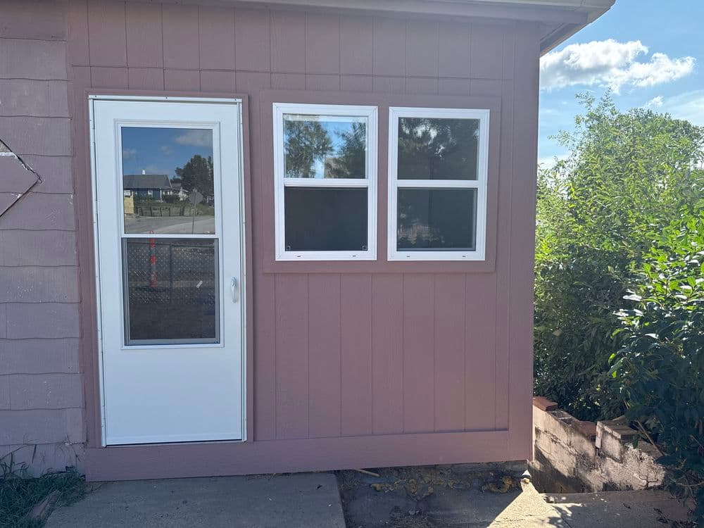 Pink exterior wall of a residential structure with a white door and two small windows.